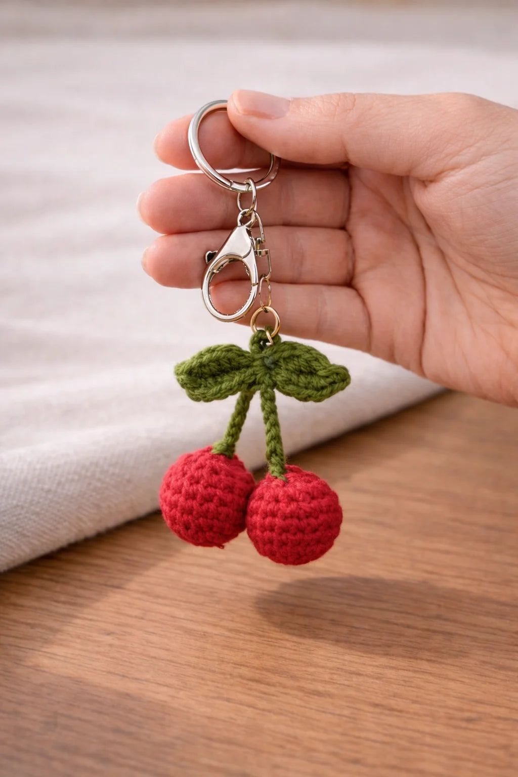 Hand holding a cherry-themed keychain on a wooden surface