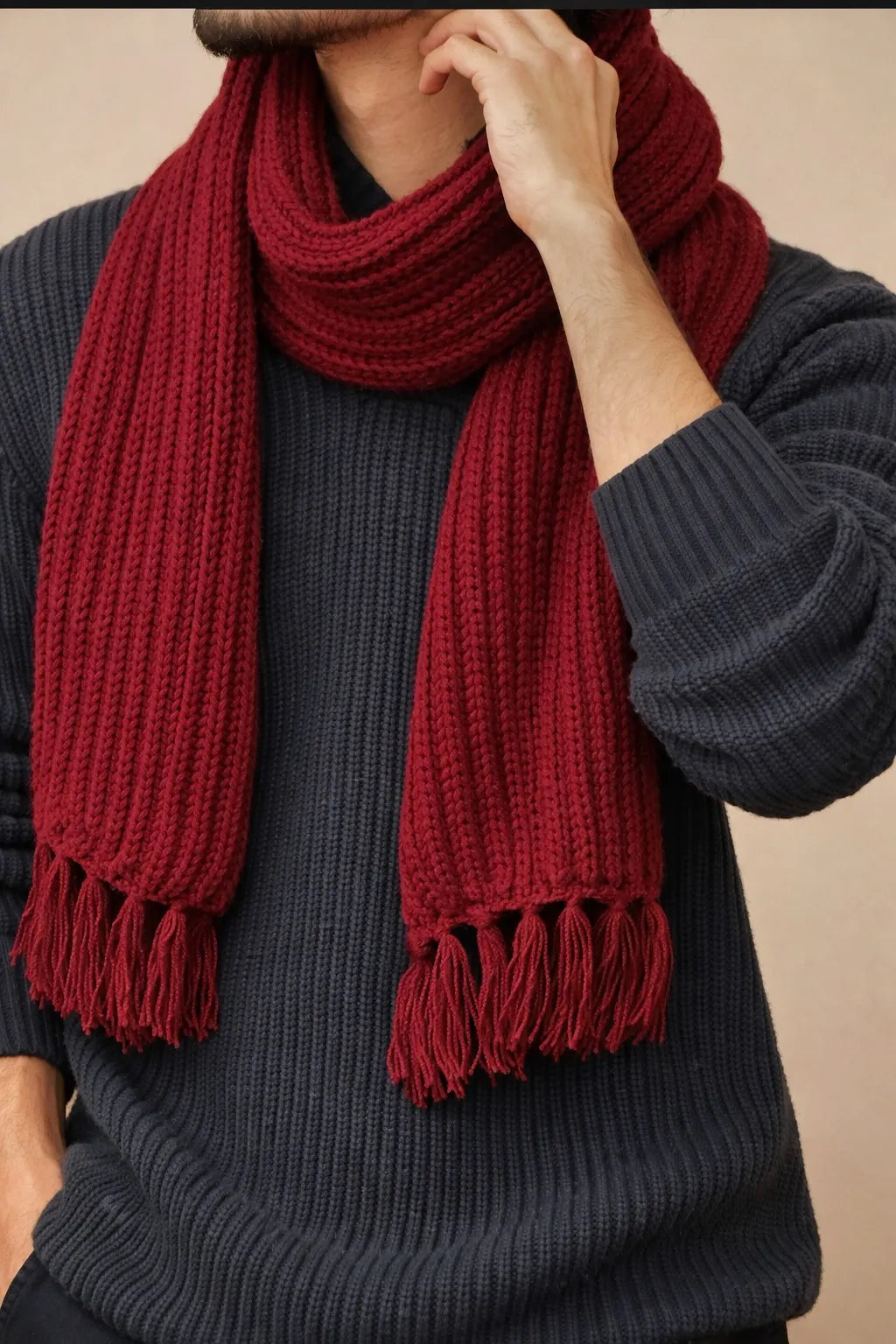 Person wearing a red knitted scarf with tassels on a neutral background