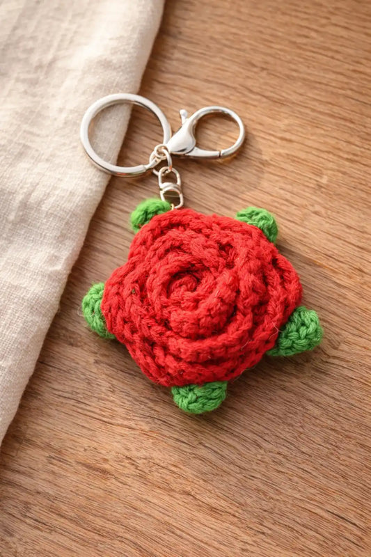 Detailed view of a red crochet rose keychain with green leaves and a silver lobster clasp on a wooden surface.