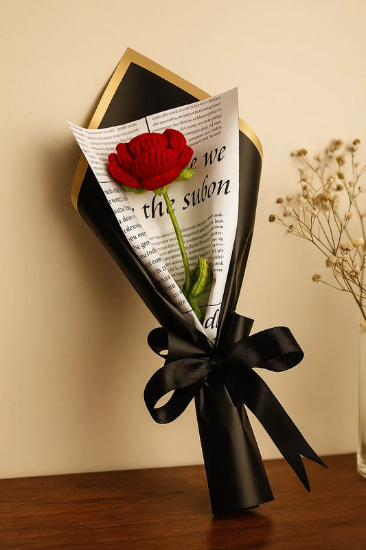 Bouquet of red rose wrapped in black paper with text, tied with a black ribbon on a wooden surface. "Single red crochet rose flower, perfect romantic gift" "Handmade single forever red rose crochet flower gift"