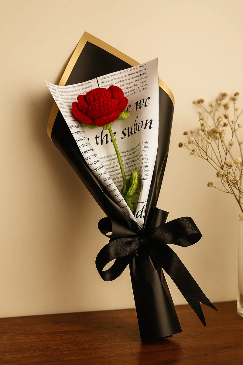 Bouquet of red rose wrapped in black paper with text, tied with a black ribbon on a wooden surface. "Single red crochet rose flower, perfect romantic gift" "Handmade single forever red rose crochet flower gift"