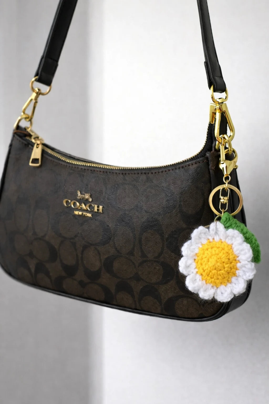 Handmade crochet white daisy keychain with yellow center and metal clasp on coach bag